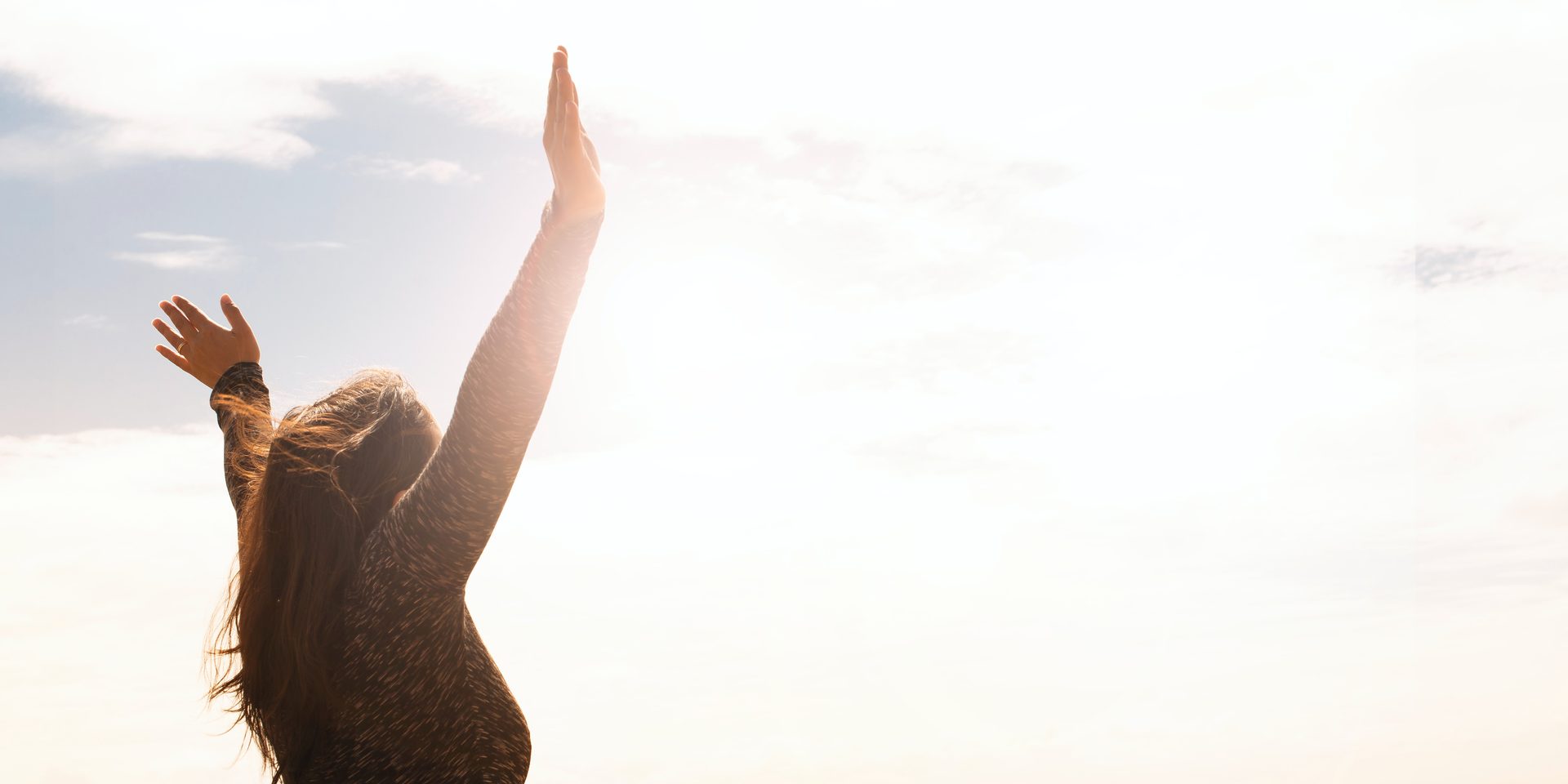 A woman on a beach raising her arm toward the sunrise