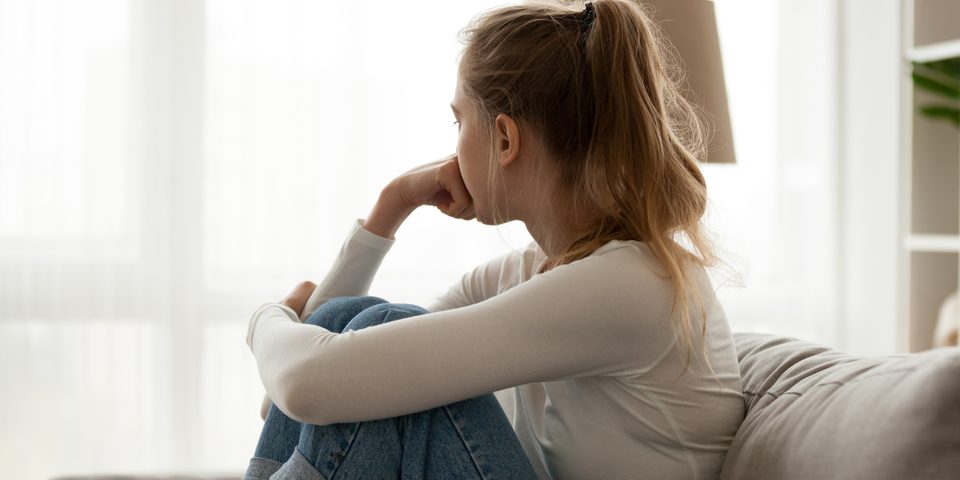A young woman sitting on a sofa by a window, lost in thought