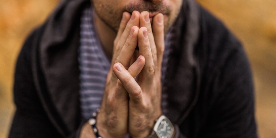 A man with his hands clasped in front of his face