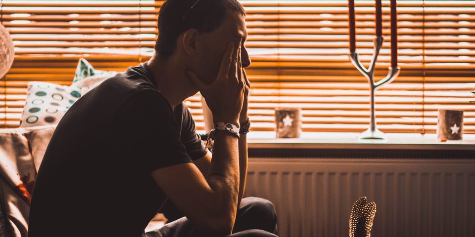 A man sitting by a window with his hand on his forehead