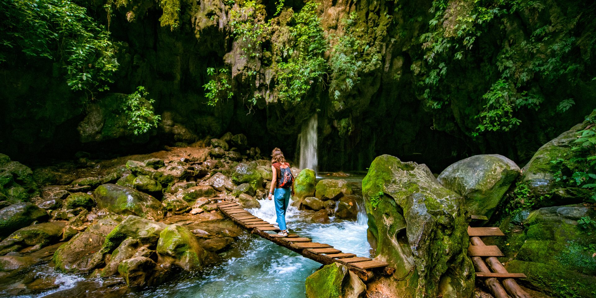 A hiker crossing a wooden footbridge over a forest stream